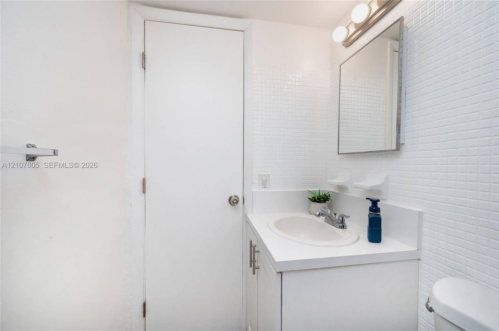 444 SW 27th Avenue, #42, Miami, Miami, FL 33135 Vanity featuring a white countertop with an integrated basin, square wall-mounted mirror, three-bulb vanity light fixture, and white grid-pattern wall tile