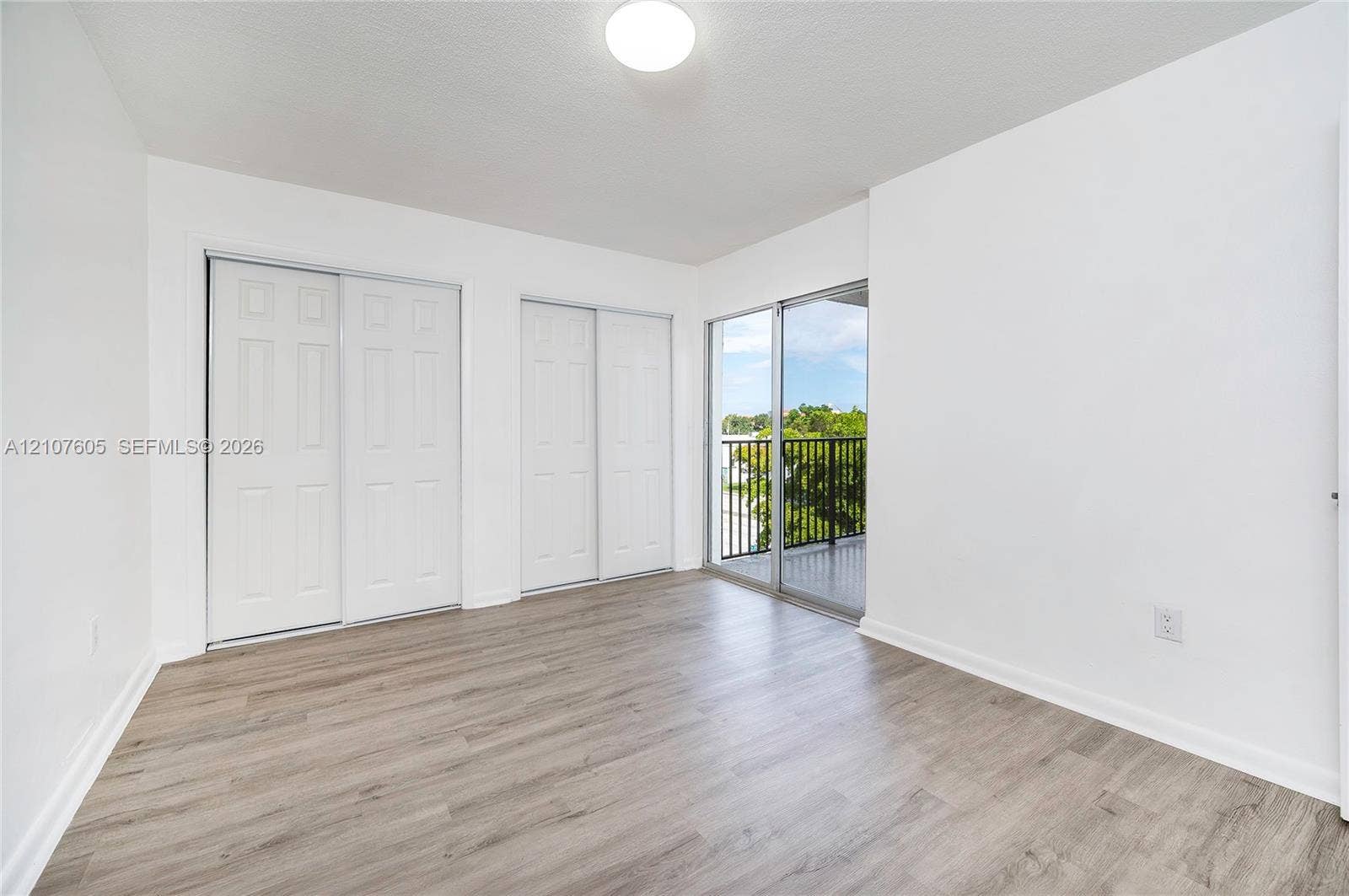444 SW 27th Avenue, #42, Miami, Miami, FL 33135 Room featuring wood-finish flooring, dual sliding-door closets with paneled detailing, and a glass sliding door providing access to an exterior balcony