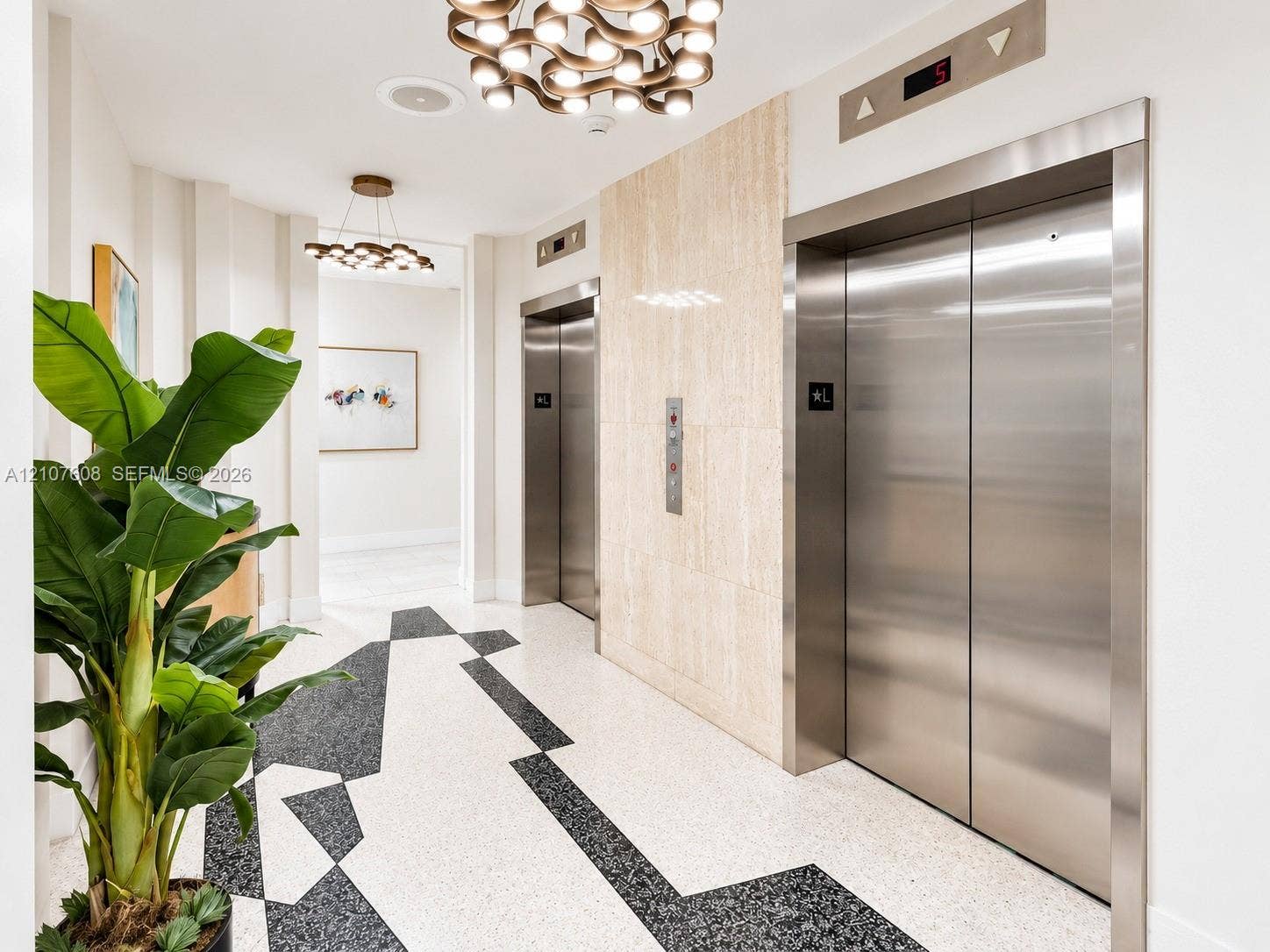2000 S Ocean Boulevard, #12F, Lauderdale-By-The-Sea, Lauderdale By The Sea, FL 33062 Elevator lobby featuring stainless steel doors, stone-tiled accent wall, geometric terrazzo flooring, and modern multi-bulb chandeliers