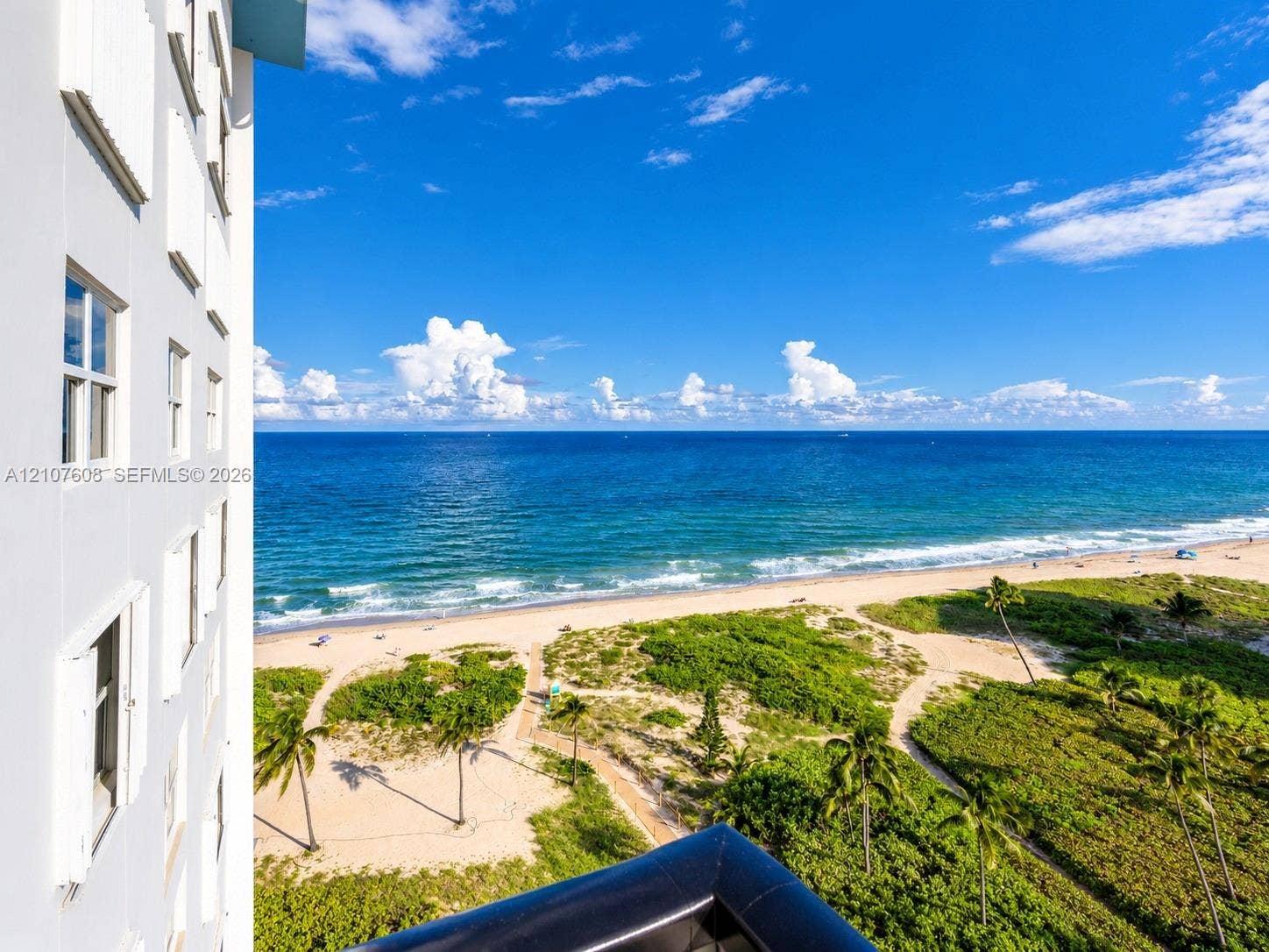 2000 S Ocean Boulevard, #12F, Lauderdale-By-The-Sea, Lauderdale By The Sea, FL 33062 High-rise building exterior featuring a balcony with a black railing, overlooking an expansive coastal shoreline, sandy beach, and native vegetation