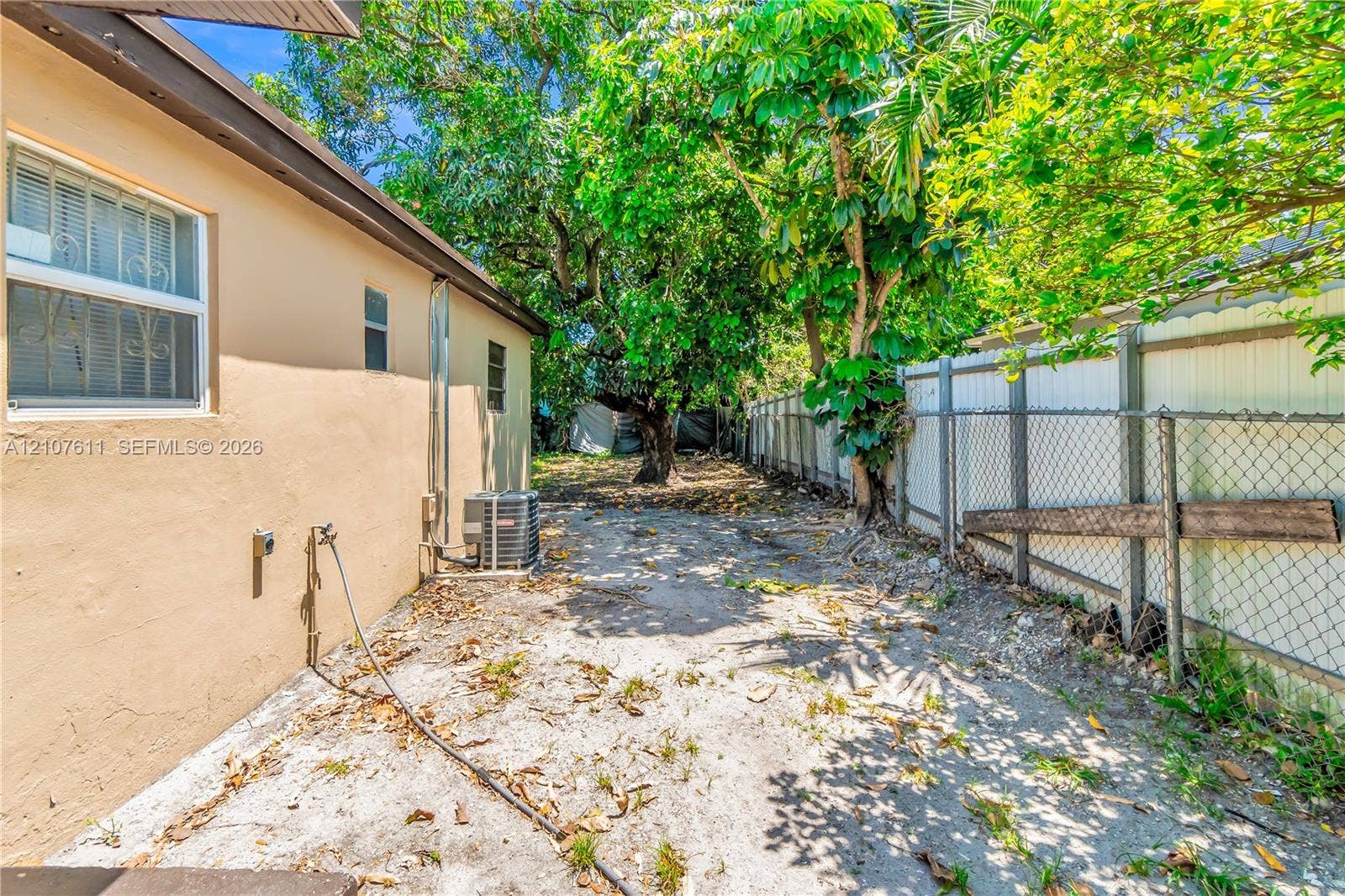 2910 NW 47th Street, Miami, FL 33142 Side exterior featuring a stucco facade, horizontal slider windows, and a chain-link fence perimeter