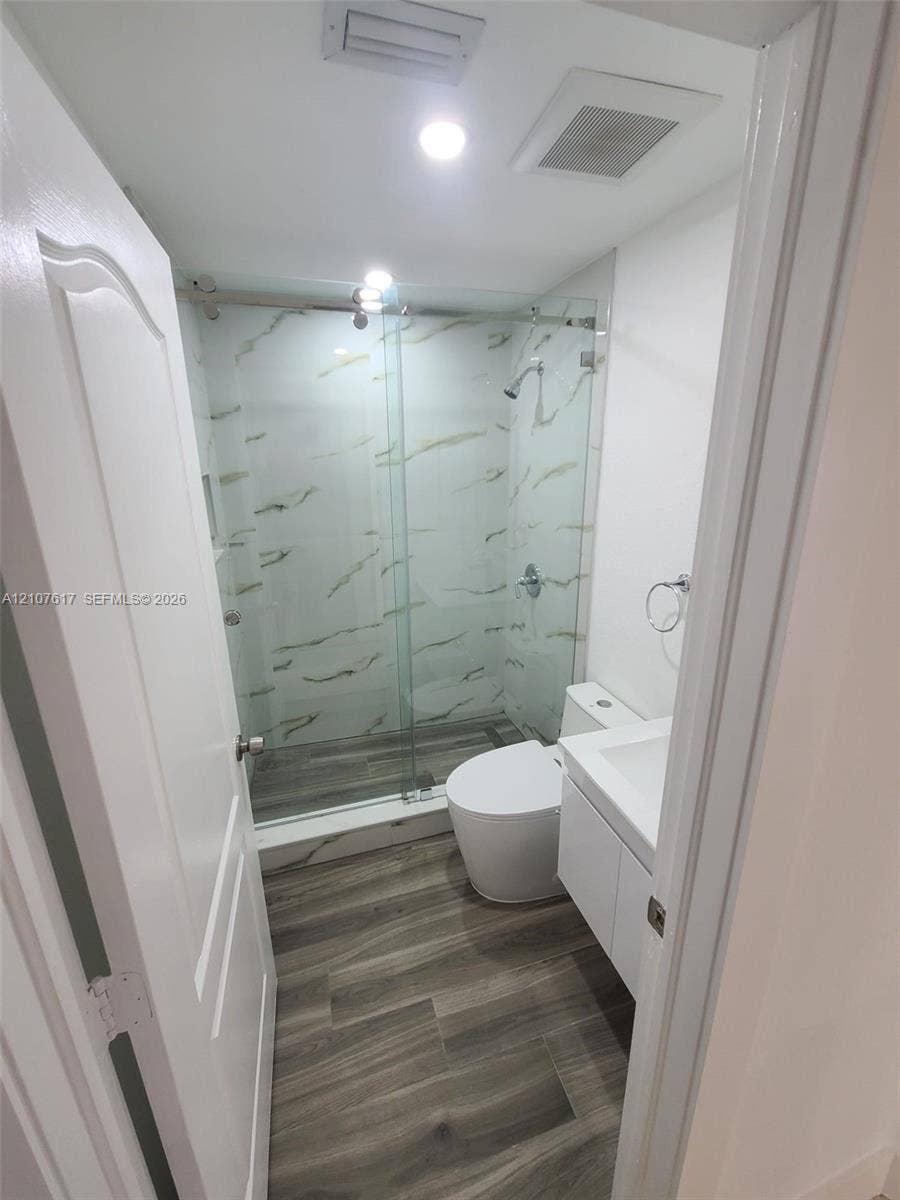 17415 NW 75th Place, #103, Hialeah, Hialeah, FL 33015 Walk-in shower with floor-to-ceiling stone-pattern tile, frameless glass sliding door, wood-finish flooring, and white floating vanity