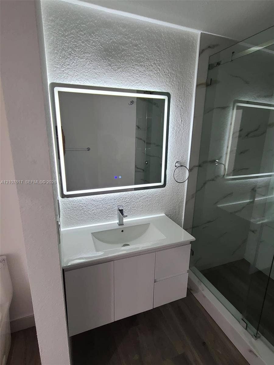 17415 NW 75th Place, #103, Hialeah, Hialeah, FL 33015 Floating vanity with white countertop and integrated sink, illuminated rectangular LED mirror, textured wall finish, and glass-enclosed shower with wall tile