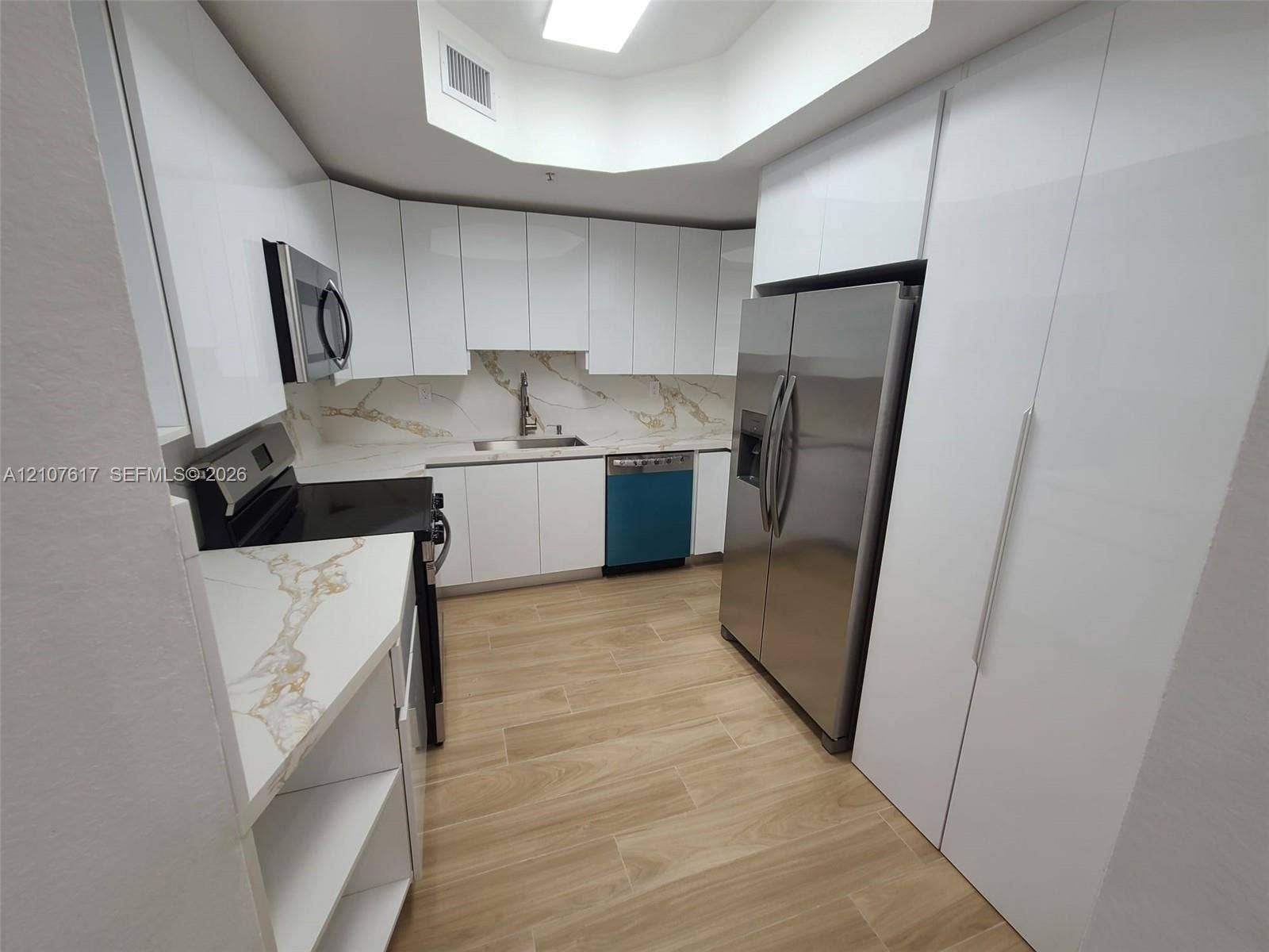 17415 NW 75th Place, #103, Hialeah, Hialeah, FL 33015 Modern kitchen featuring high-gloss white cabinetry, stone-finish countertops and backsplash, integrated stainless steel appliances, and wood-finish flooring under a recessed ceiling light fixture