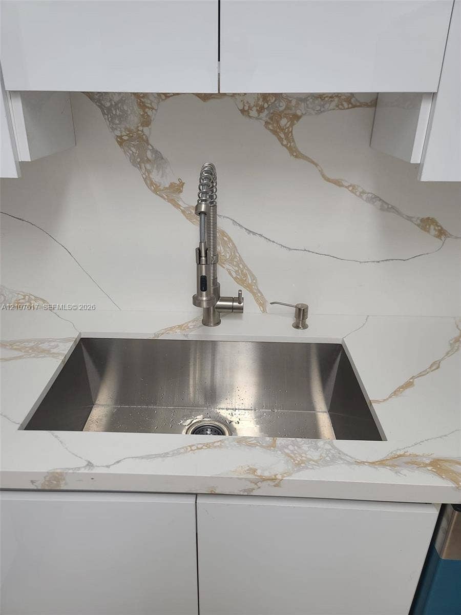 17415 NW 75th Place, #103, Hialeah, Hialeah, FL 33015 Undermount stainless steel sink featuring a high-arc pull-down sprayer faucet, integrated soap dispenser, and patterned stone-finish countertop and backsplash with white high-gloss cabinetry