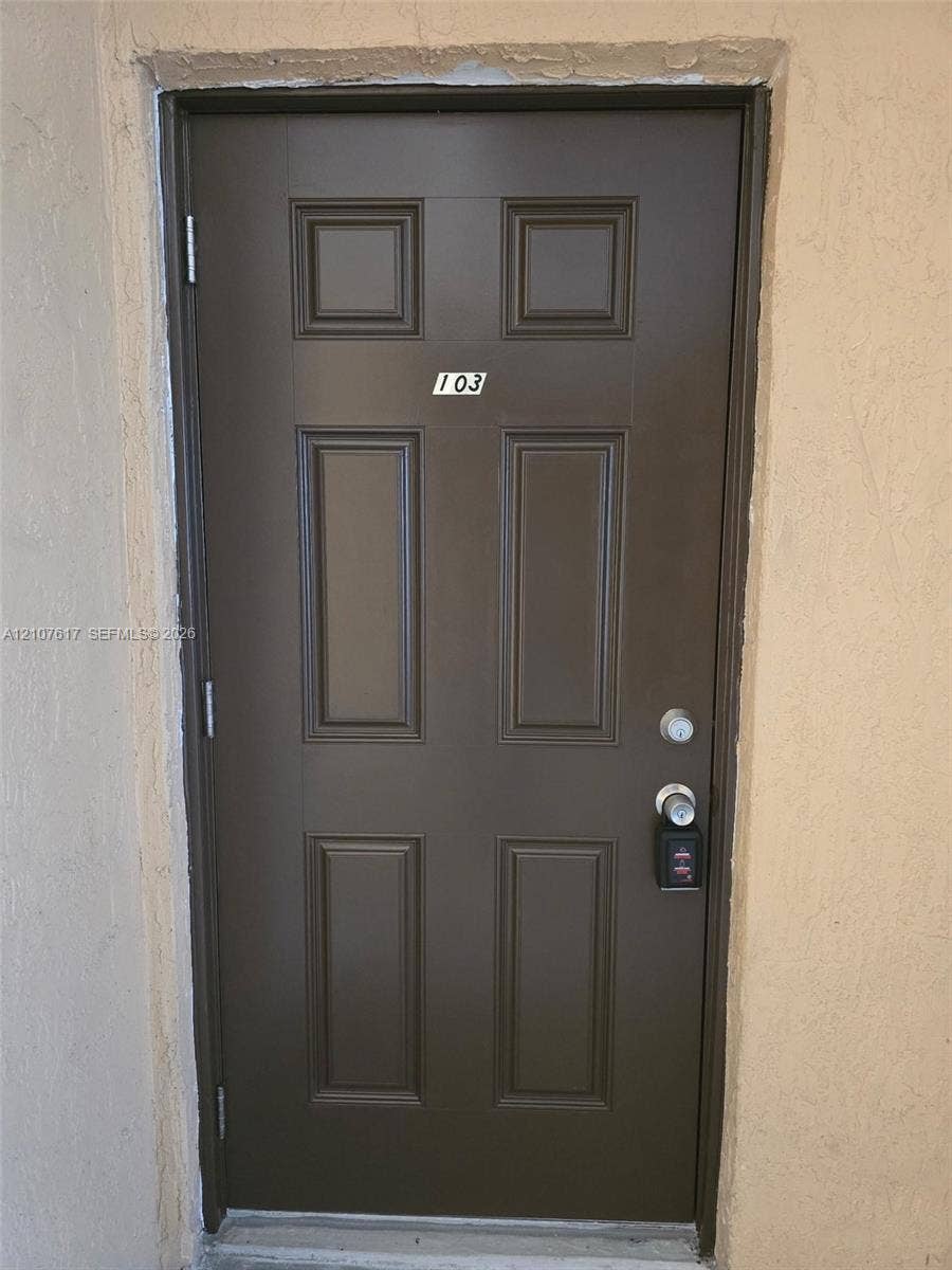 17415 NW 75th Place, #103, Hialeah, Hialeah, FL 33015 Six-panel brown entry door featuring a dual-lock system and textured wall surround