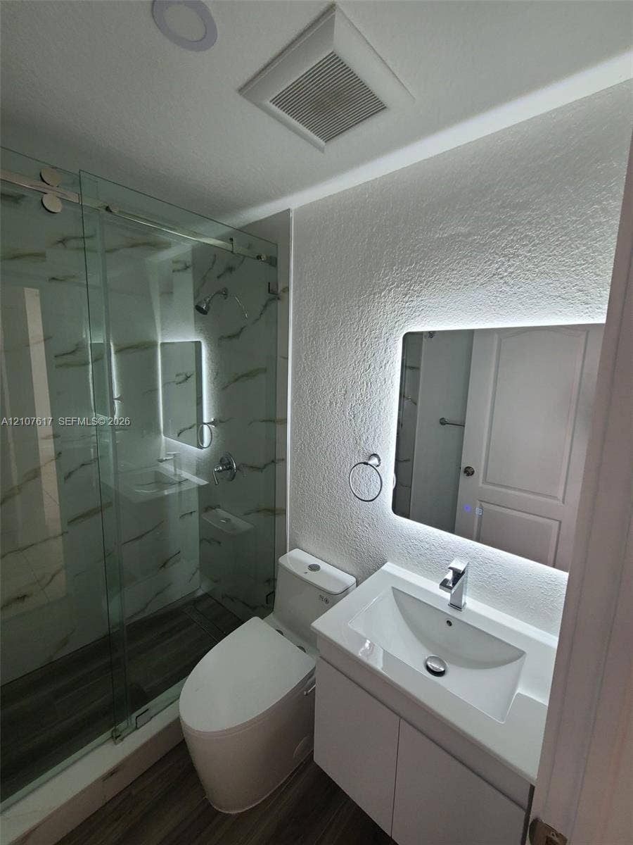 17415 NW 75th Place, #103, Hialeah, Hialeah, FL 33015 Glass-enclosed shower with tiled walls, modern vanity with rectangular basin, back-lit mirror, and wood-finish flooring