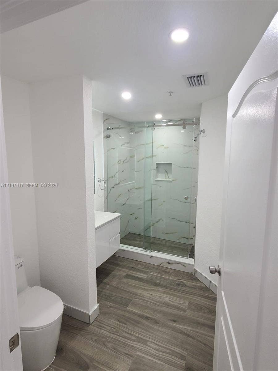 17415 NW 75th Place, #103, Hialeah, Hialeah, FL 33015 Walk-in glass-enclosed shower with tiled surround and built-in niche, wood-finish flooring, white floating vanity, and recessed lighting