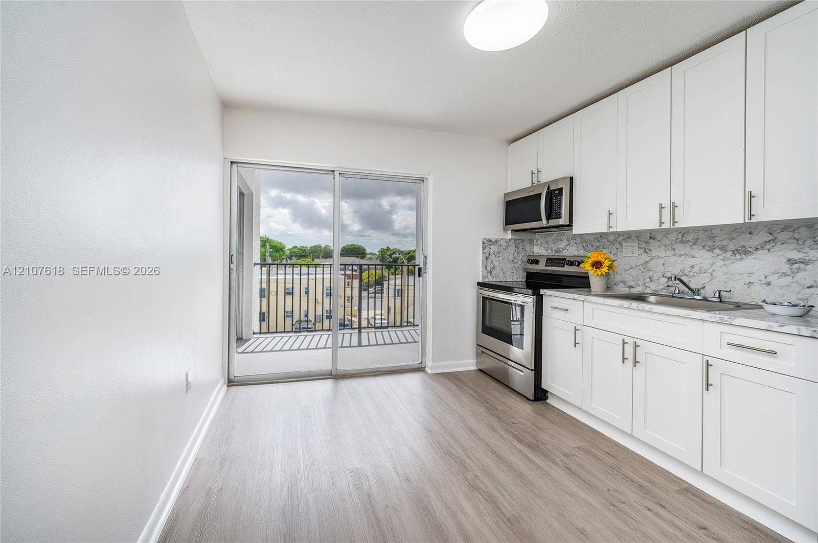 444 SW 27th Avenue, #46, Miami, Miami, FL 33135 Kitchen featuring white cabinetry, stainless steel appliances, patterned stone-look backsplash, wood-finish flooring, and sliding glass doors leading to a private balcony