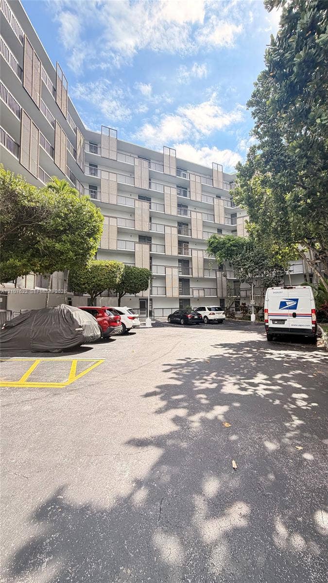 20400 W Country Club Drive, #112, Aventura, FL 33180 Mid-rise building exterior featuring a white facade, staggered balcony dividers, glass railings, and on-site surface parking