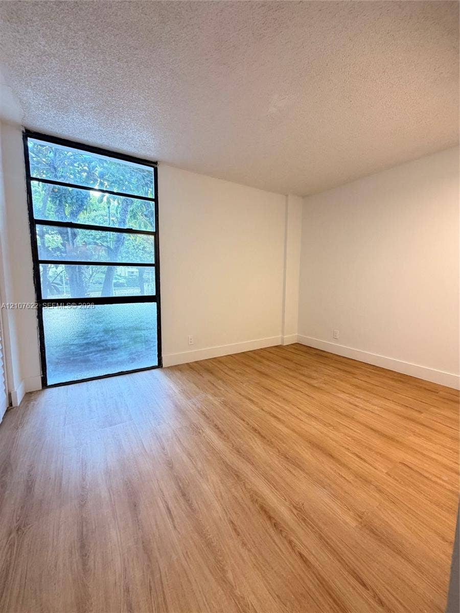 20400 W Country Club Drive, #112, Aventura, FL 33180 Room interior featuring wood-finish flooring, white walls, and a large multi-pane window with a black frame