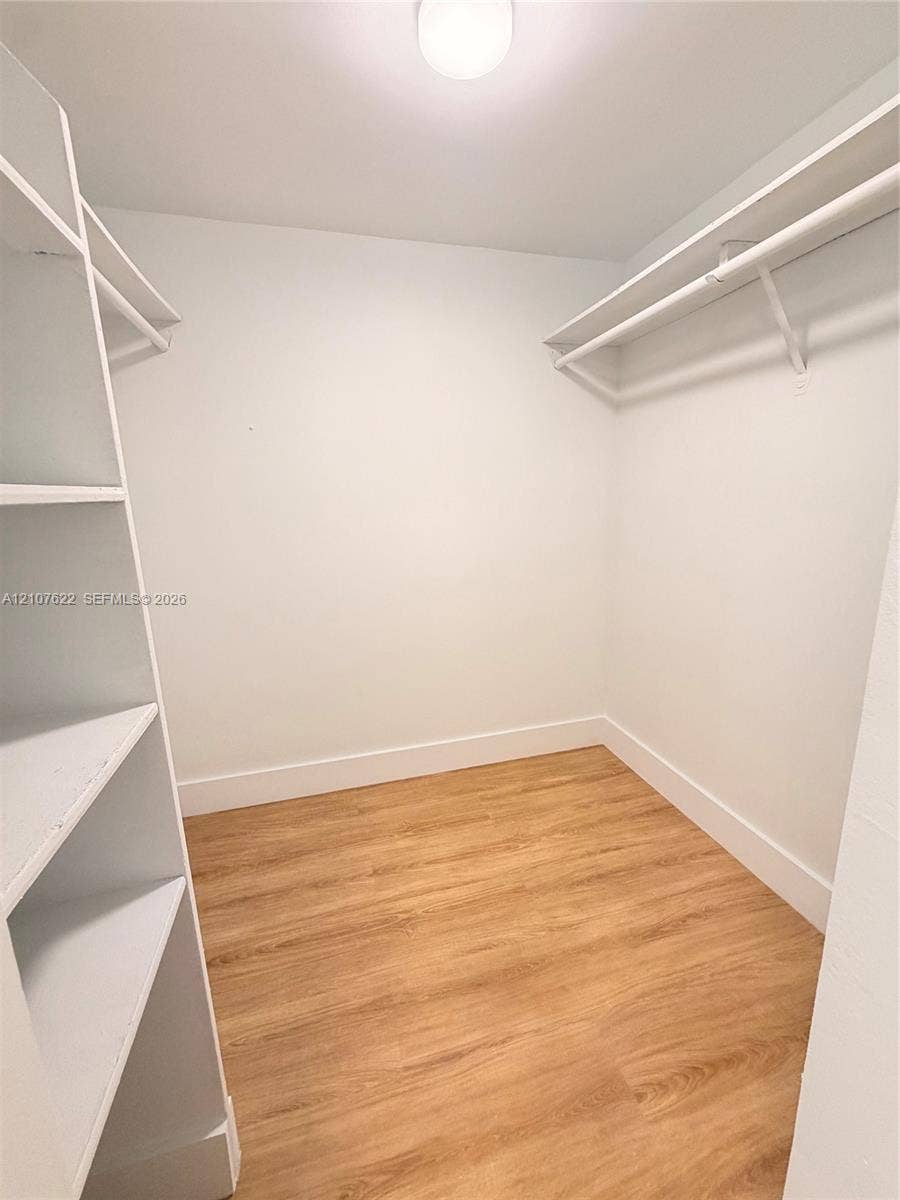 20400 W Country Club Drive, #112, Aventura, FL 33180 Walk-in closet featuring white built-in shelving, white overhead hanging rods, wood-finish flooring, and a central ceiling light fixture