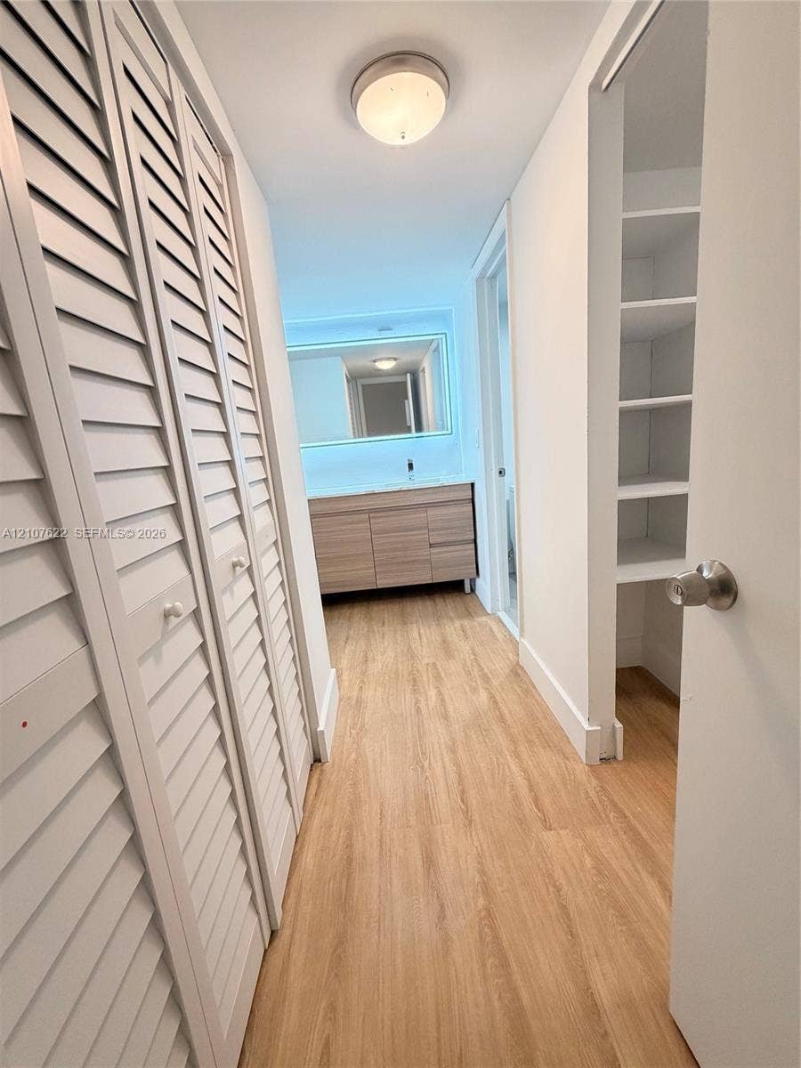 20400 W Country Club Drive, #112, Aventura, FL 33180 Wood-finish flooring, white louvered-style closet doors, built-in open shelving, vanity with integrated cabinetry, and an illuminated vanity mirror