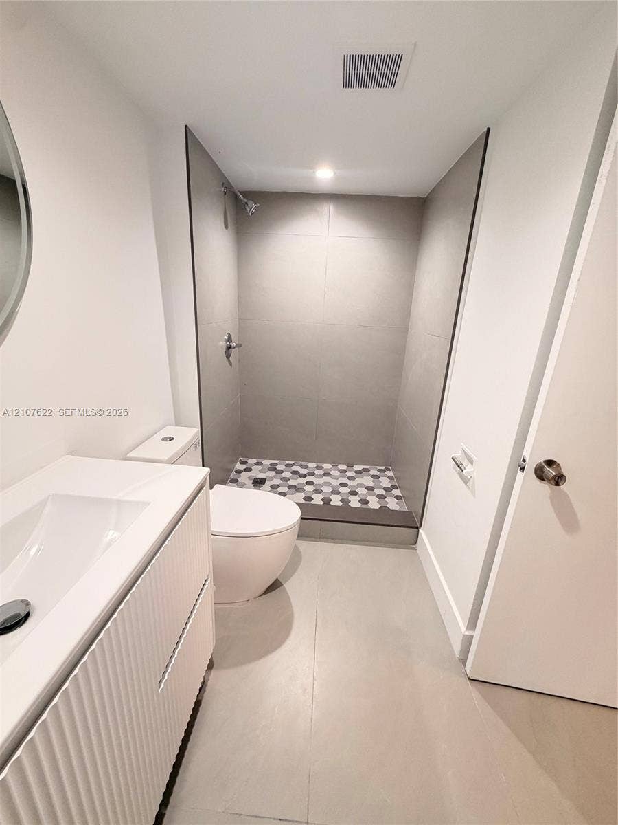 20400 W Country Club Drive, #112, Aventura, FL 33180 Bathroom featuring a white fluted-front vanity with an integrated sink, floor-to-ceiling large-format wall tiling, and a shower floor finished with hexagonal mosaic tiles