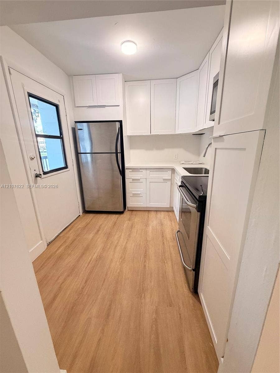 20400 W Country Club Drive, #112, Aventura, FL 33180 Kitchen featuring white shaker-style cabinetry, wood-finish flooring, stainless steel appliances, and solid surface countertops