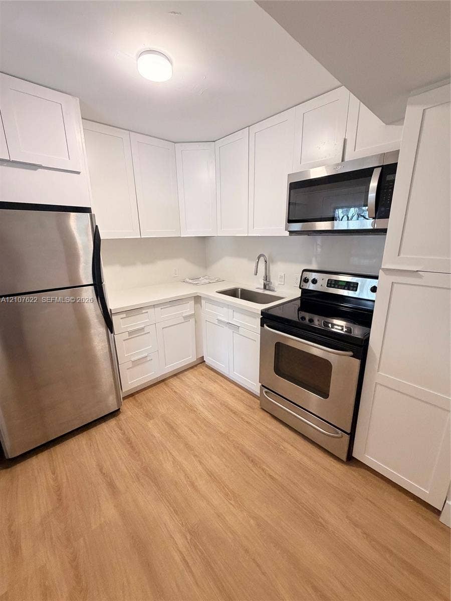 20400 W Country Club Drive, #112, Aventura, FL 33180 Kitchen featuring white shaker-style cabinetry, solid-surface countertops, stainless steel appliances, and wood-finish flooring
