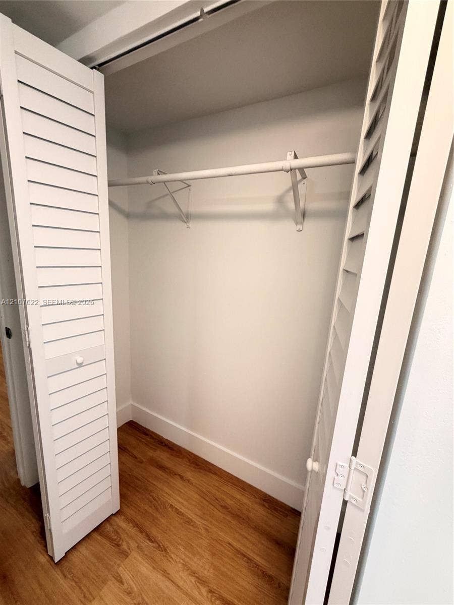 20400 W Country Club Drive, #112, Aventura, FL 33180 Storage closet featuring white louvered bifold doors, wood-finish flooring, and a metal hanging rod