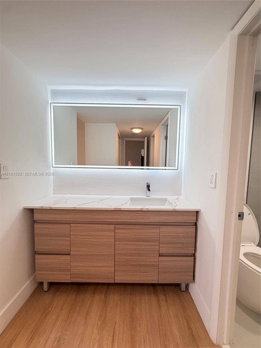 20400 W Country Club Drive, #112, Aventura, FL 33180 Wood-finish vanity with four drawers and dual cabinet doors, quartz countertop with integrated sink, chrome faucet, and rectangular LED-backlit mirror