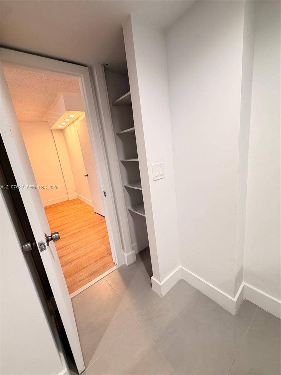 20400 W Country Club Drive, #112, Aventura, FL 33180 Interior space featuring large-format ceramic floor tile, built-in recessed shelving, and a wood-finish floor beyond a doorway with brushed metal hardware