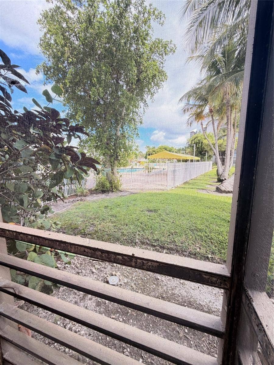 20400 W Country Club Drive, #112, Aventura, FL 33180 Screened enclosure overlooking a grass lawn, mature palm trees, perimeter fencing, and a swimming pool