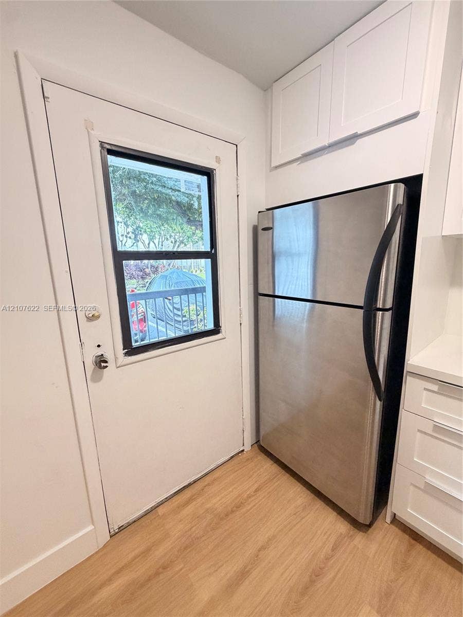 20400 W Country Club Drive, #112, Aventura, FL 33180 Stainless steel refrigerator, white cabinetry with overhead storage, wood-finish flooring, and a single-light exterior door