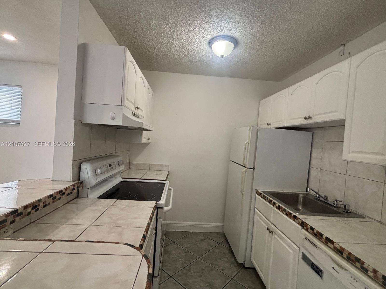 19 Crossings Circle, #H, Boynton Beach, Boynton Beach, FL 33435 Kitchen featuring white cabinetry, tile countertops with decorative mosaic backsplash, tile flooring, and a stainless steel sink