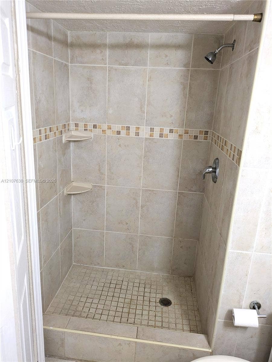 Walk-in shower featuring ceramic wall tile, a decorative glass mosaic tile border, integrated corner shelving, and a mosaic tile floor
