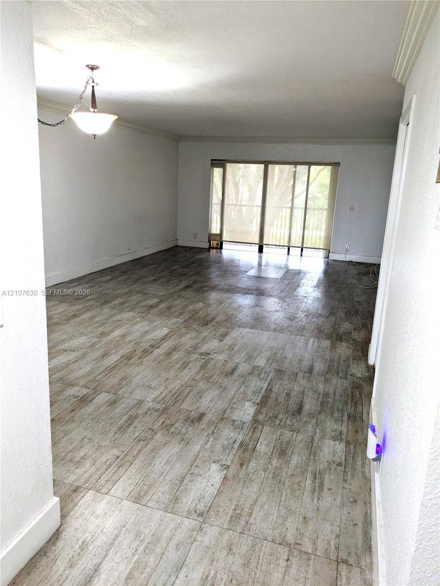 Open-concept interior featuring wood-finish tile flooring, a multi-light pendant fixture, and sliding glass doors with balcony access