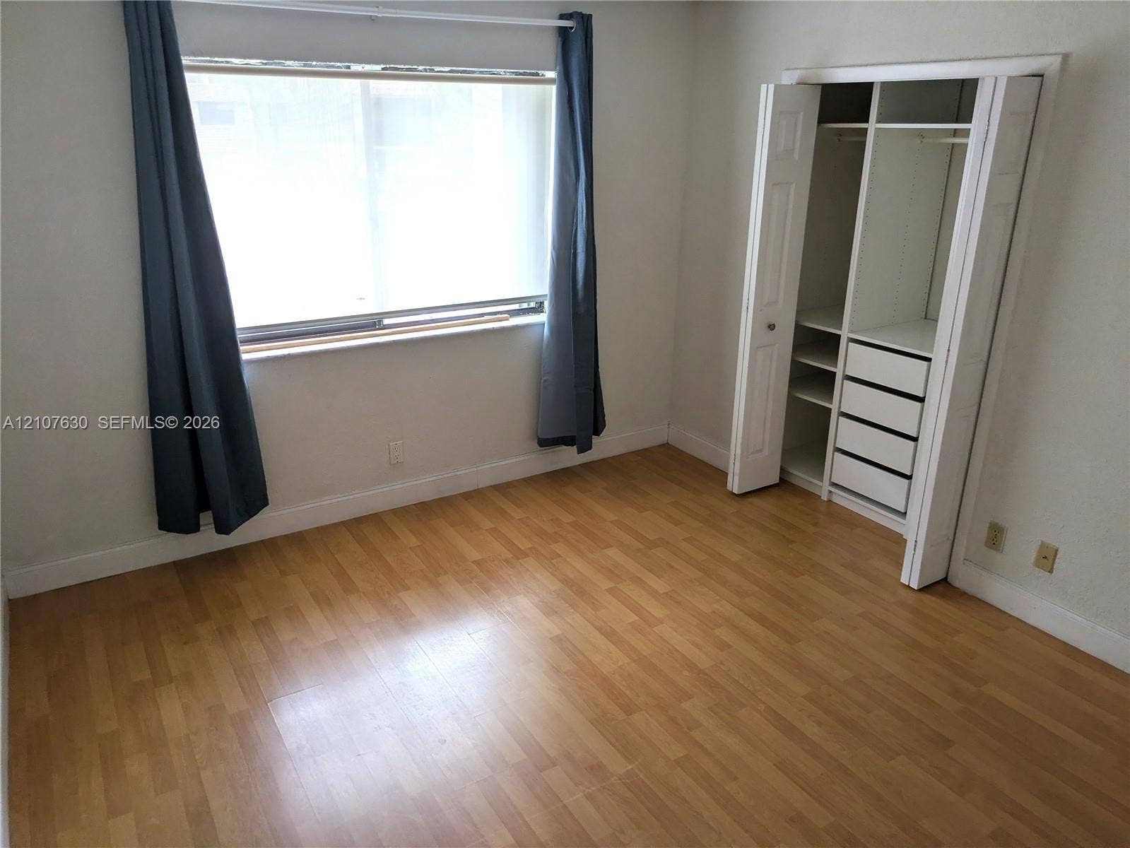 Room featuring wood-finish flooring, a large window, and a built-in closet system with integrated shelving and drawers