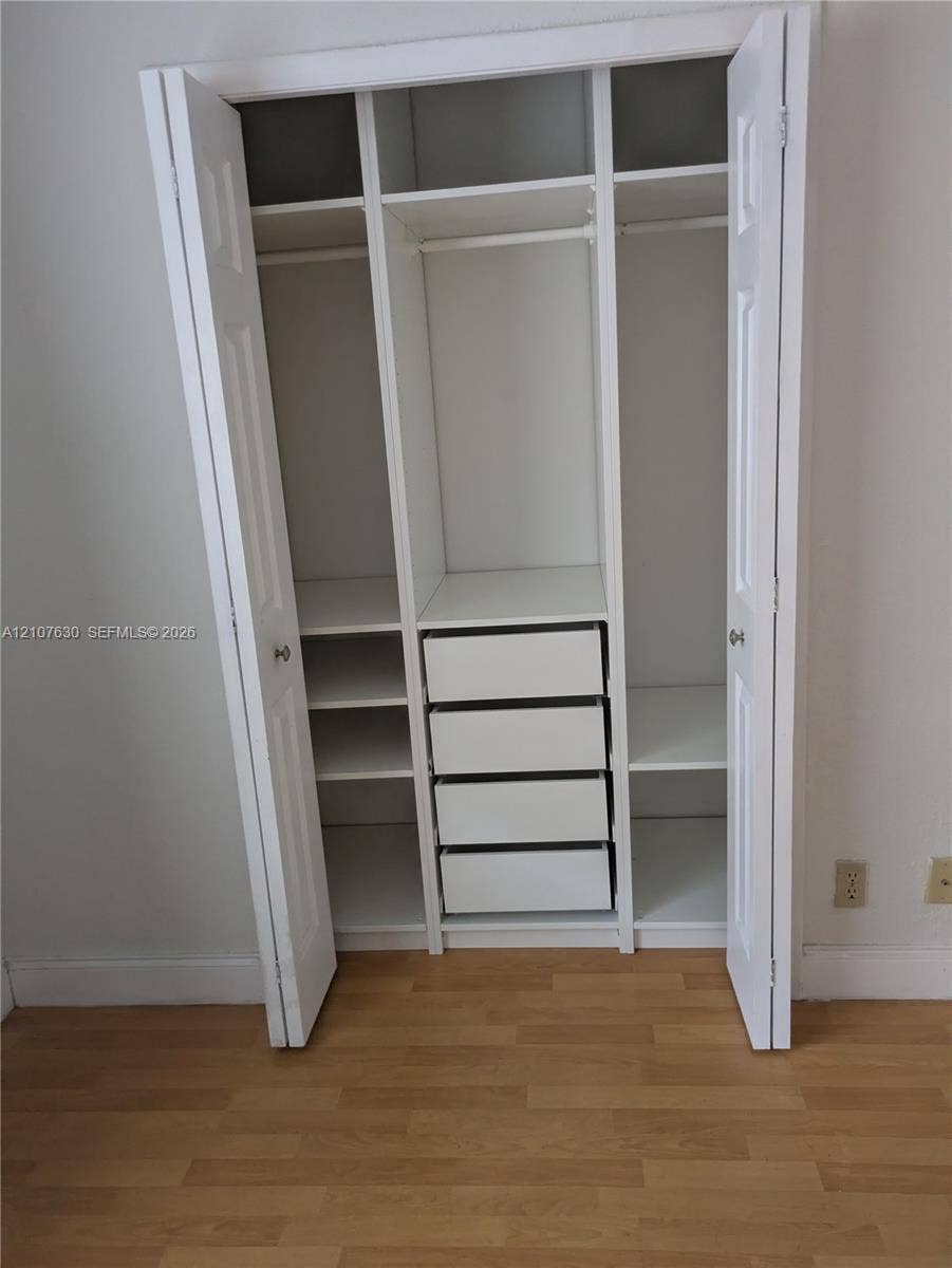 Built-in closet featuring white double-panel doors, integrated shelving, four stacked drawers, and wood-finish flooring