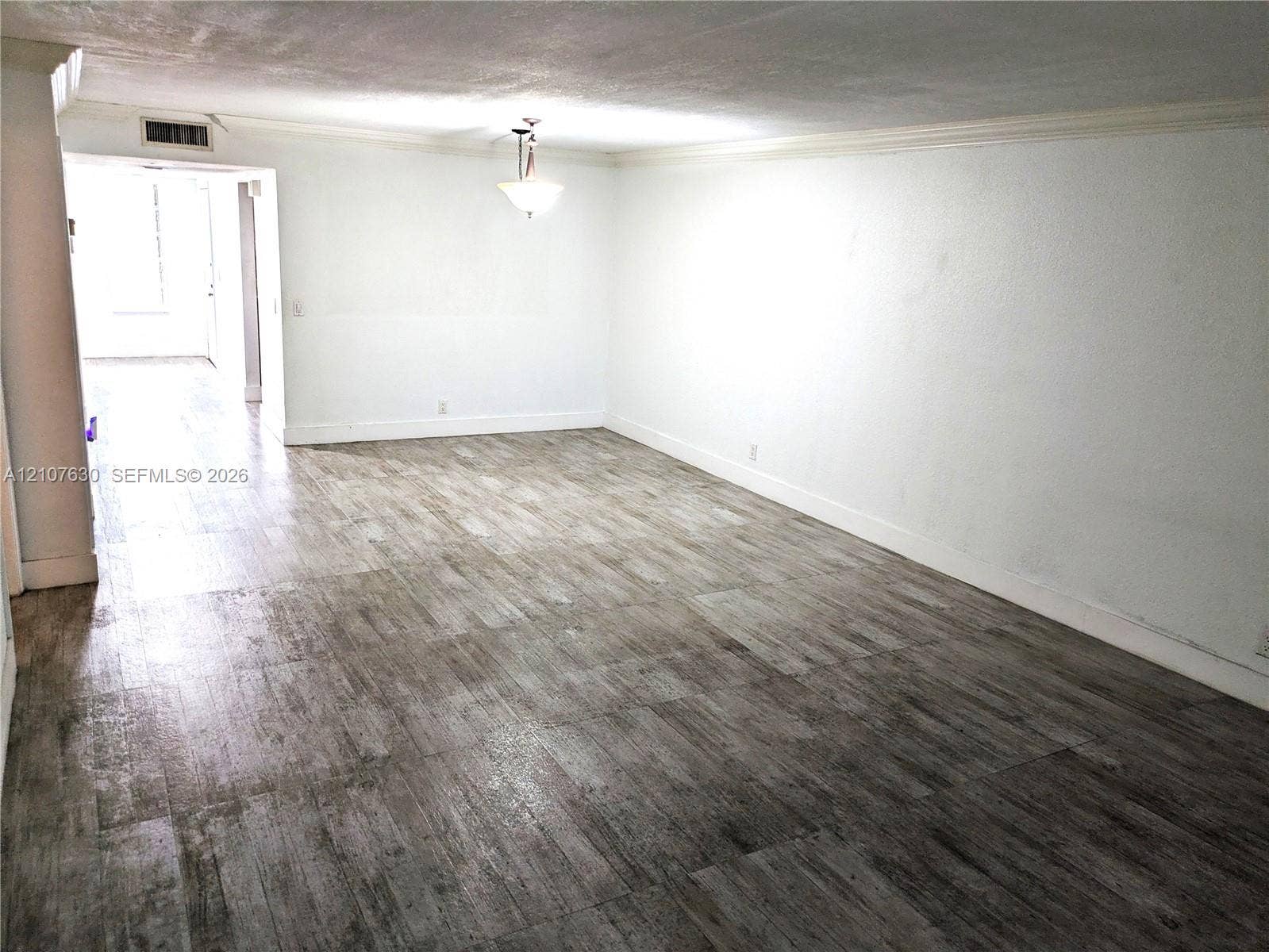 Wood-finish flooring, neutral wall tones, crown molding, and a central pendant light fixture