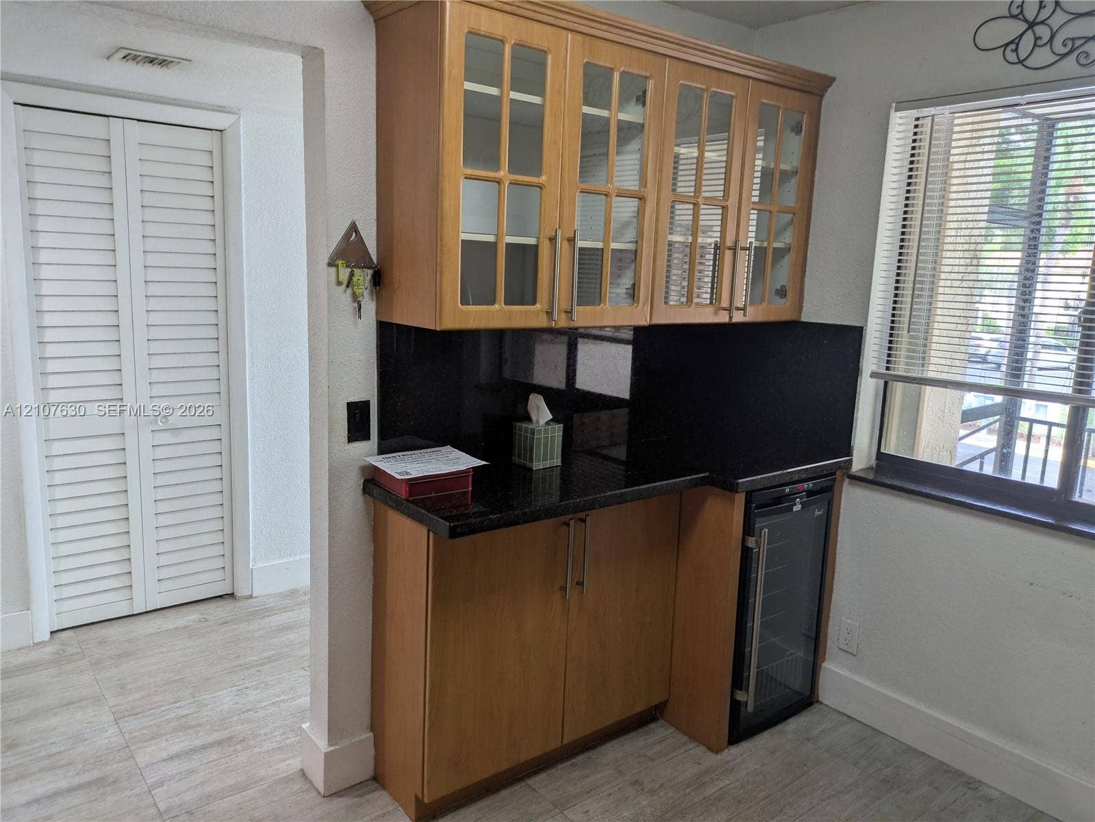 Built-in cabinetry with glass-front upper doors, dark stone-finish countertops, integrated beverage refrigerator, and light wood-finish flooring