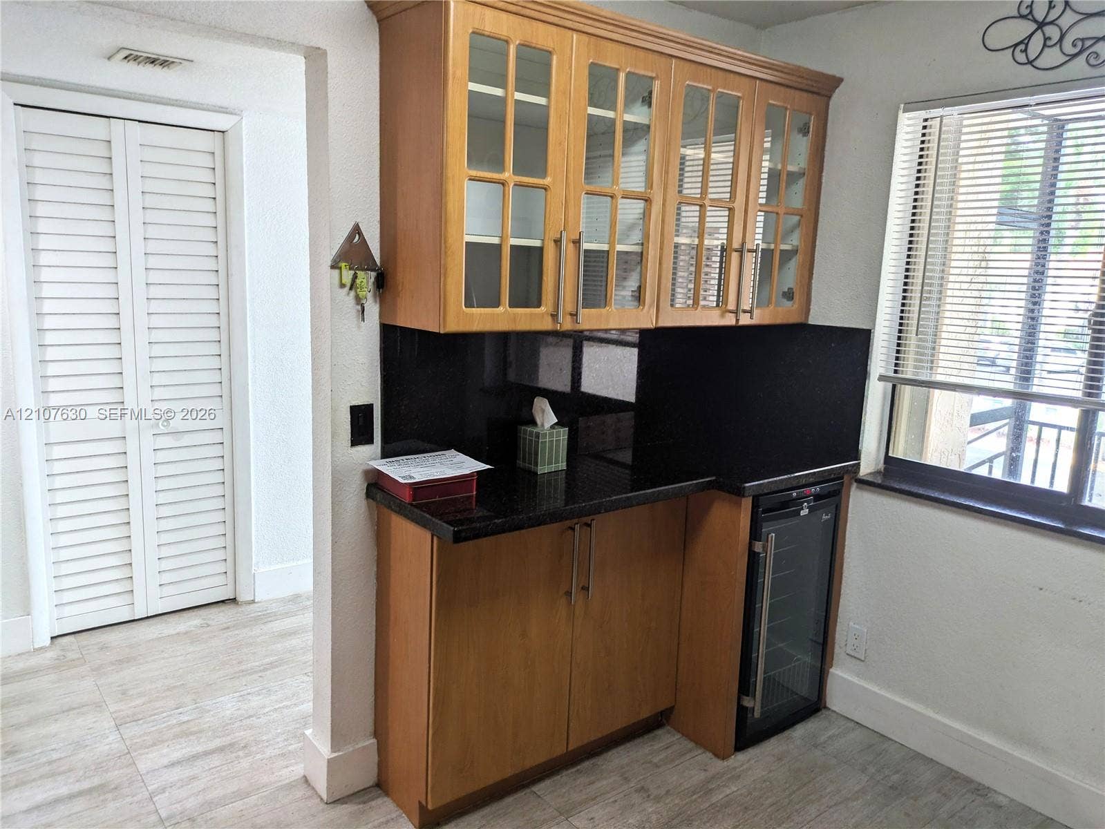 Wet bar featuring wood cabinetry with glass-front upper doors, dark stone countertops, integrated beverage refrigerator, and wood-finish flooring