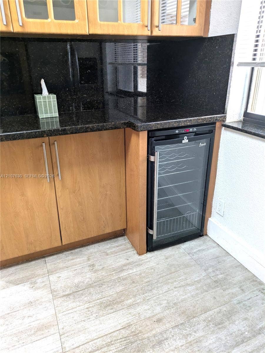 Cabinetry with glass-fronted uppers, dark stone countertops, matching backsplash, and built-in wine refrigeration