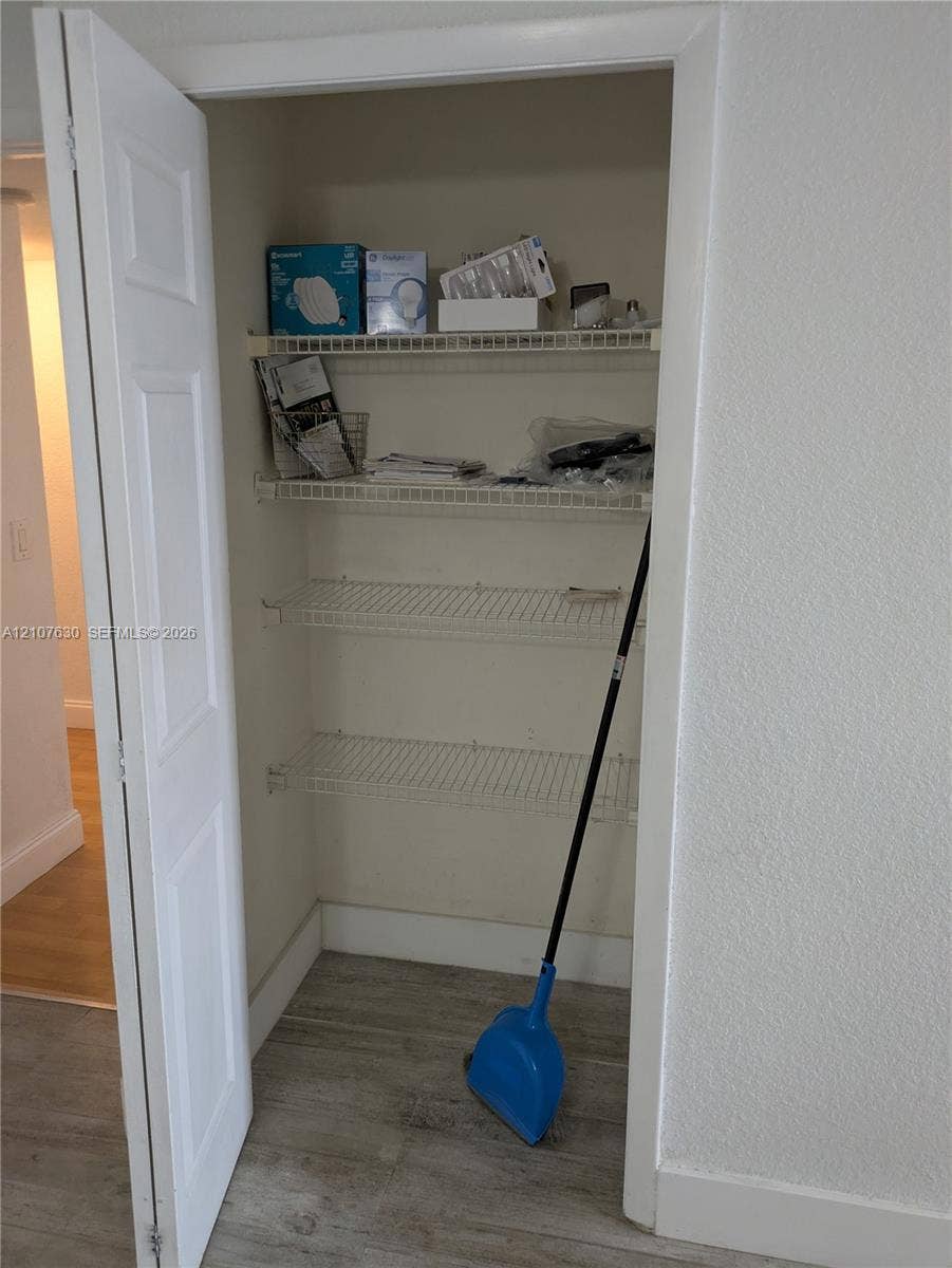 Storage closet featuring four tiers of white wire shelving and wood-finish flooring