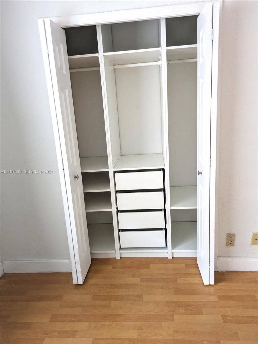 Built-in closet featuring white cabinetry, multiple overhead storage shelves, integrated hanging rods, and four pull-out drawers