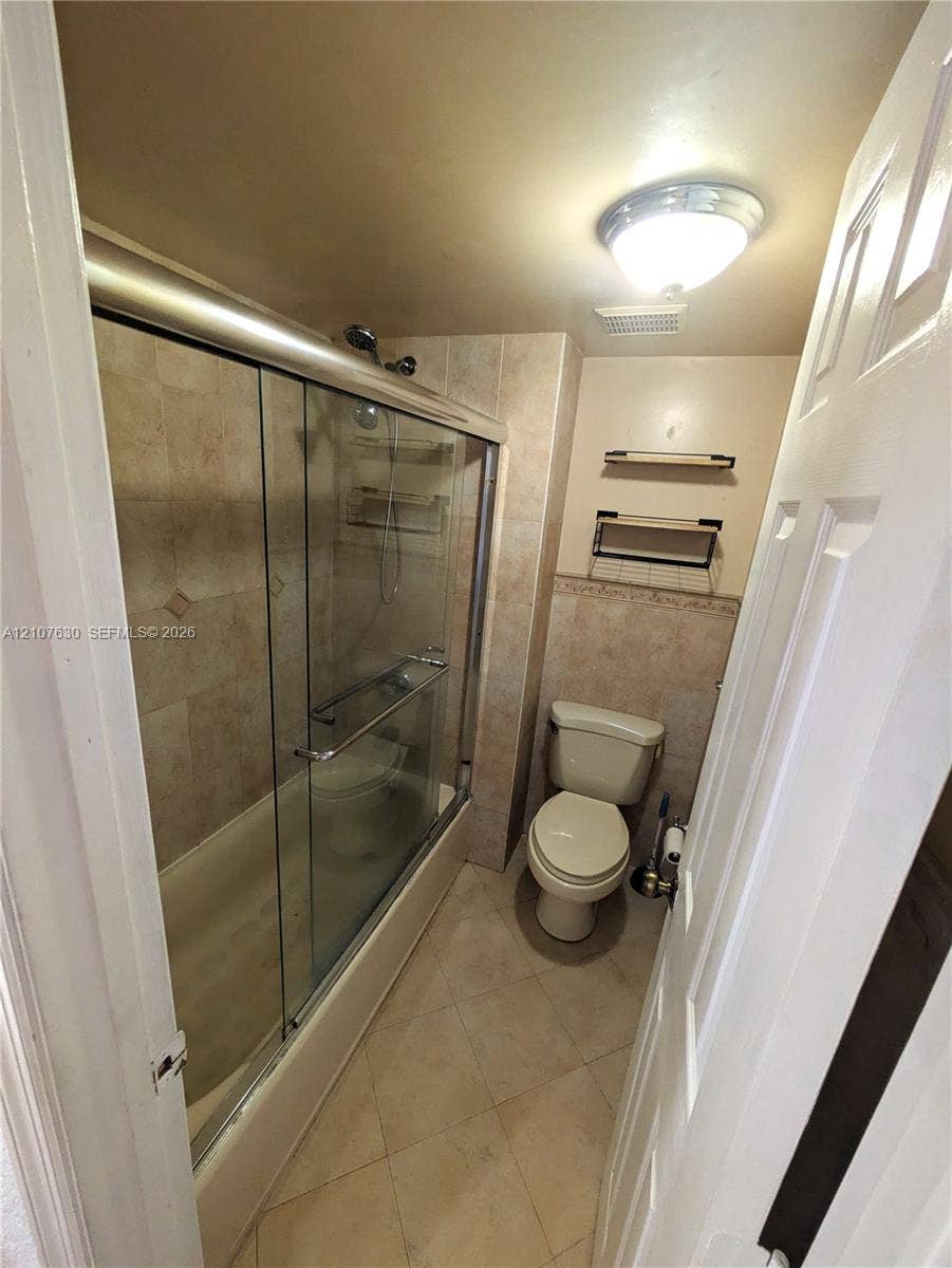Bathroom featuring a tub-shower combination with glass sliding doors, tile-surround walls, integrated shelving, and wall-mounted storage units