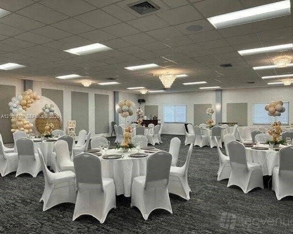 Expansive event hall featuring a drop ceiling with integrated recessed lighting, multiple crystal-style chandeliers, neutral-toned wall panels, and wall-to-wall carpeting