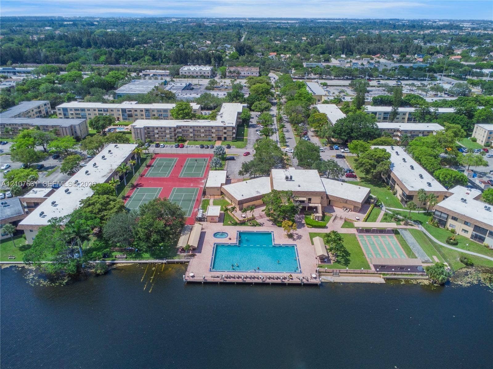 151 Berkley Road, #112, Hollywood, FL 33024 Aerial perspective featuring a waterfront swimming pool, multiple tennis courts, paved walkways, and mature landscaping