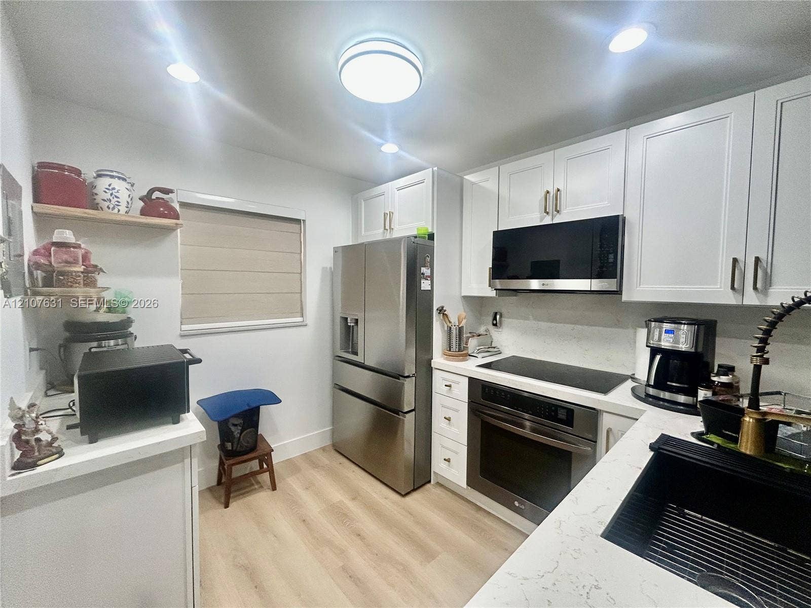 151 Berkley Road, #112, Hollywood, FL 33024 Kitchen featuring white shaker-style cabinetry, stainless steel appliances, light-toned stone-finish countertops, wood-finish flooring, and a black undermount sink with a gooseneck faucet
