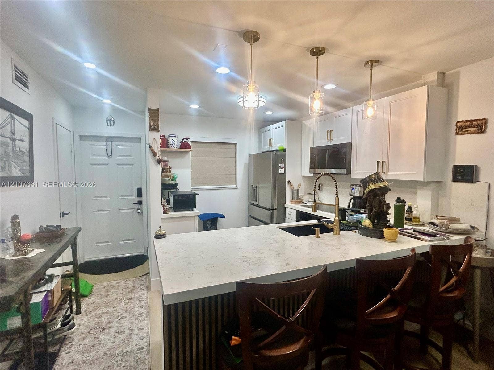 151 Berkley Road, #112, Hollywood, FL 33024 Kitchen featuring an expansive peninsula with a light-toned solid surface countertop, white shaker-style cabinetry, a brass-toned gooseneck faucet, stainless steel appliances, and tiered pendant lighting