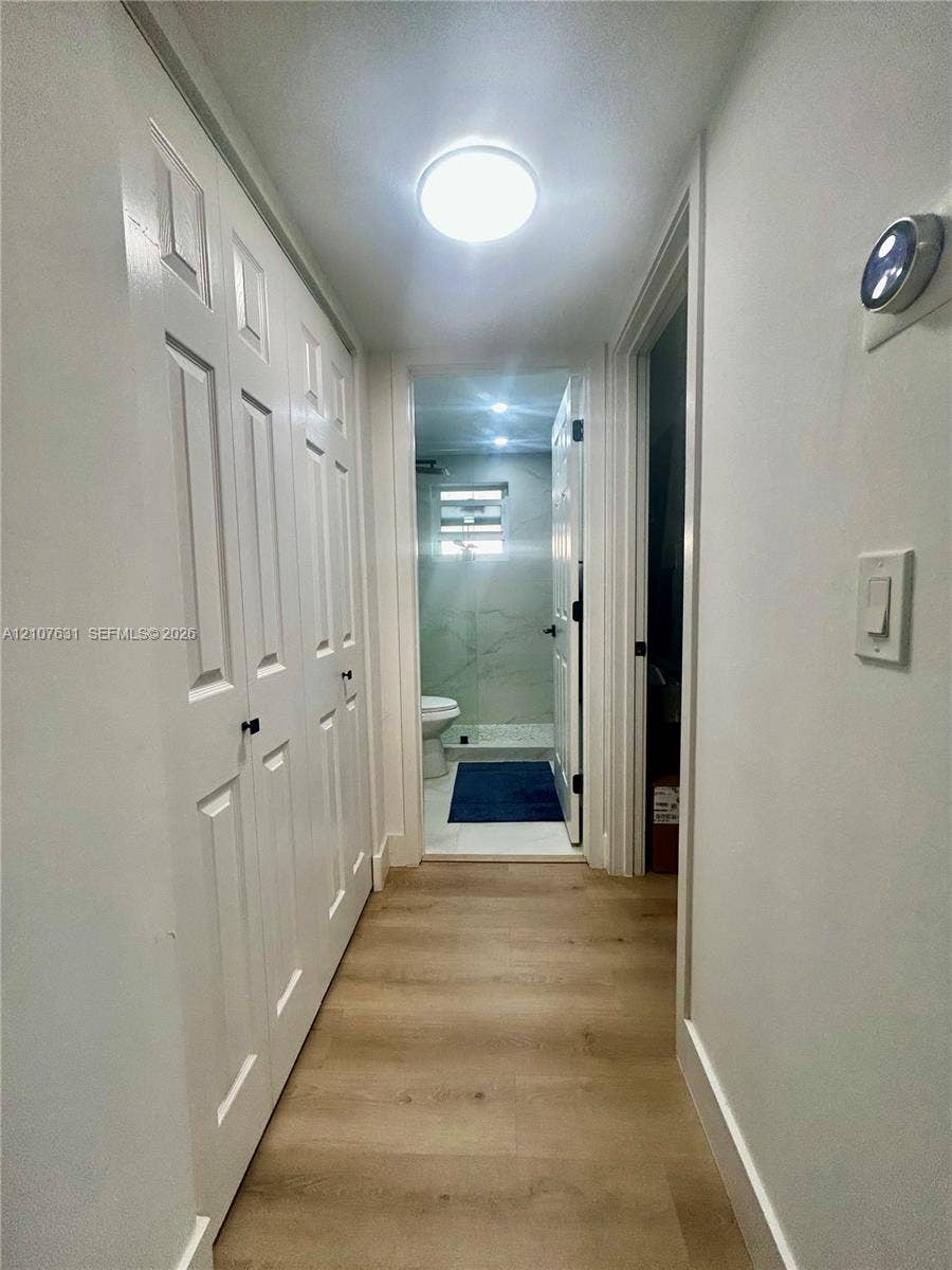 151 Berkley Road, #112, Hollywood, FL 33024 Hallway featuring wood-finish flooring, white panel-style closet doors with matte black hardware, and a flush-mount ceiling light fixture