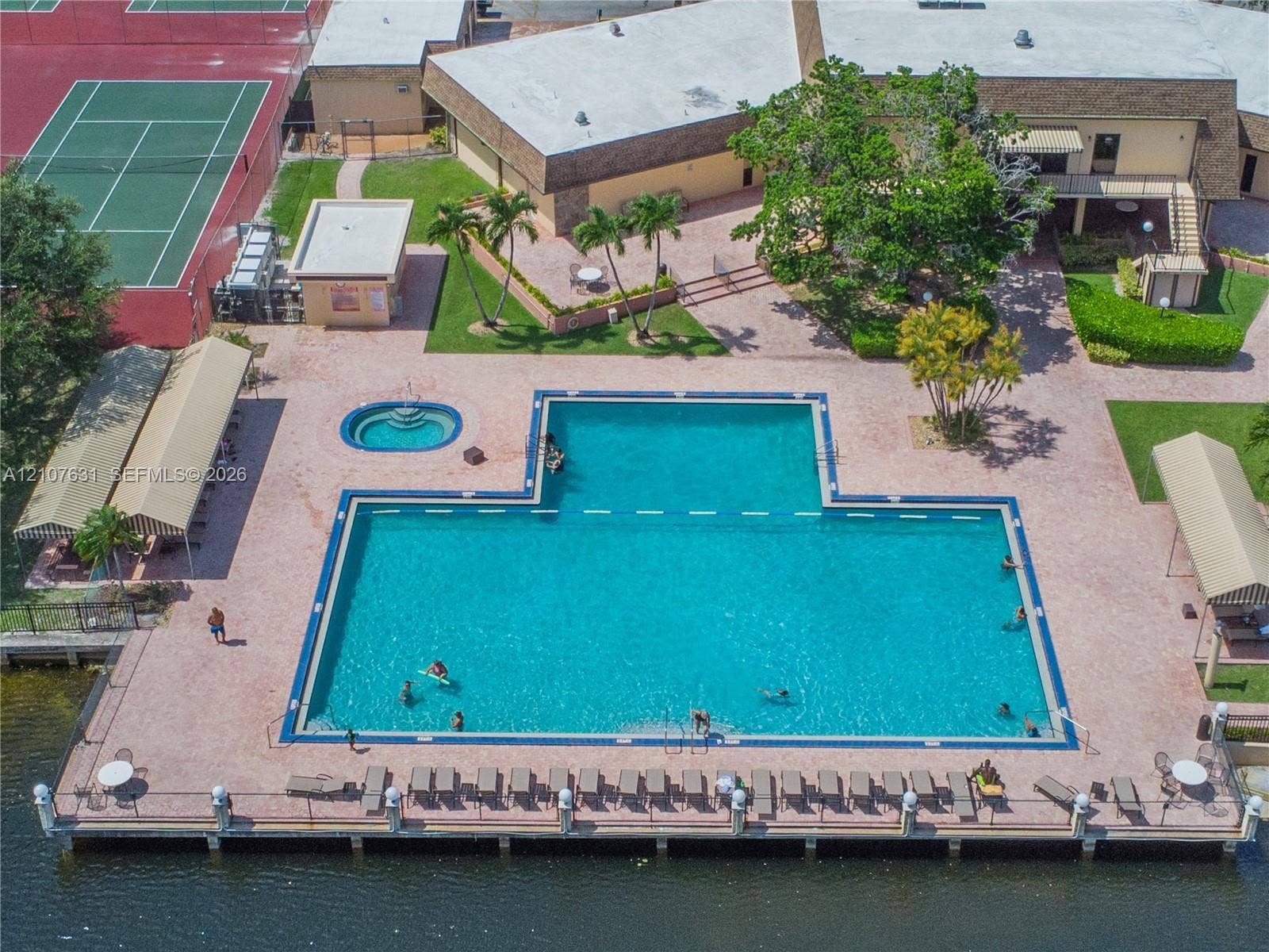 151 Berkley Road, #112, Hollywood, FL 33024 Waterfront recreational area featuring an expansive swimming pool, a dedicated spa, paved poolside decking, dual tennis courts, and covered shade structures