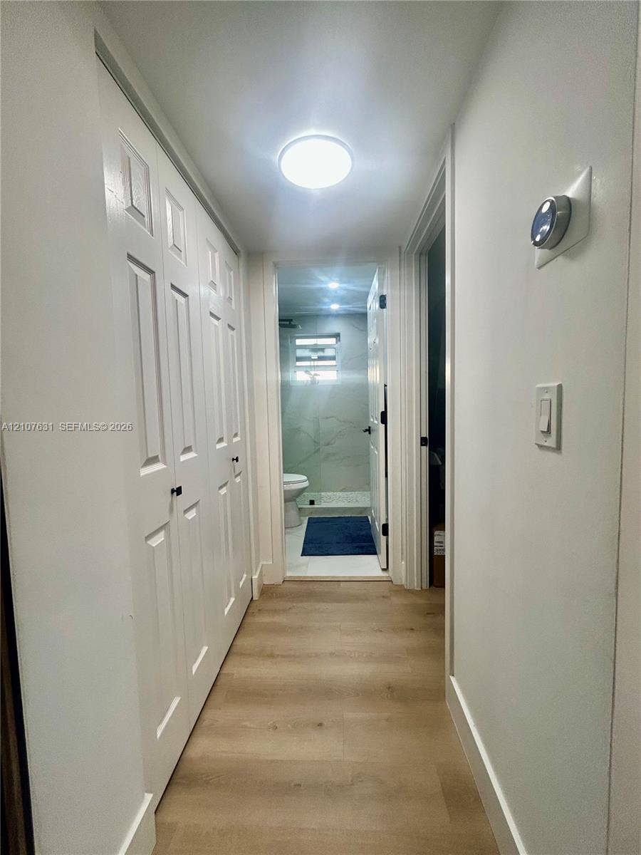 151 Berkley Road, #112, Hollywood, FL 33024 Hallway featuring wood-finish flooring, white paneled doors, ceiling-mounted lighting, and a wall-mounted digital thermostat