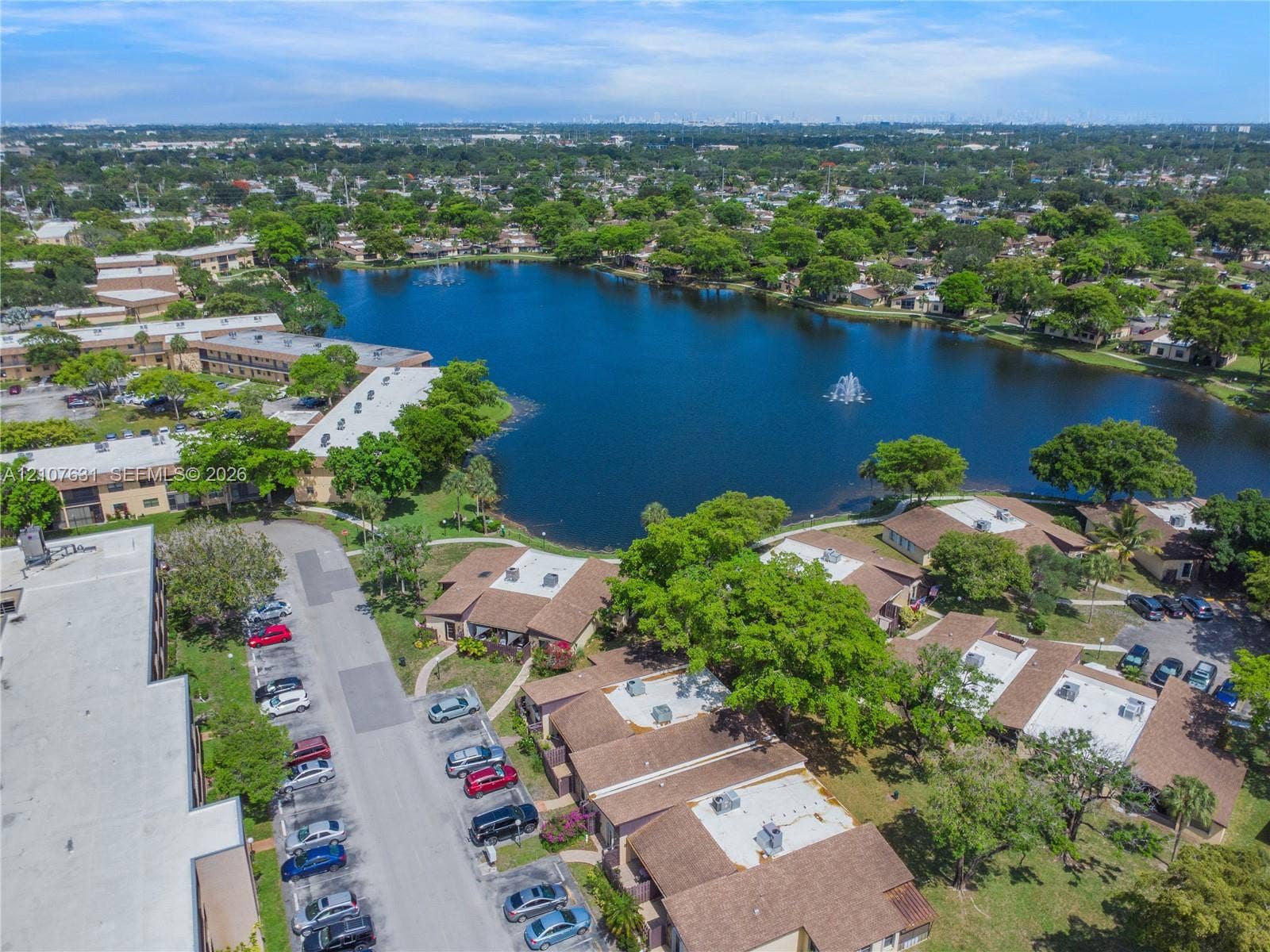 151 Berkley Road, #112, Hollywood, FL 33024 Aerial perspective featuring a multi-building residential complex, a central lake with a fountain, mature trees, and designated surface parking areas