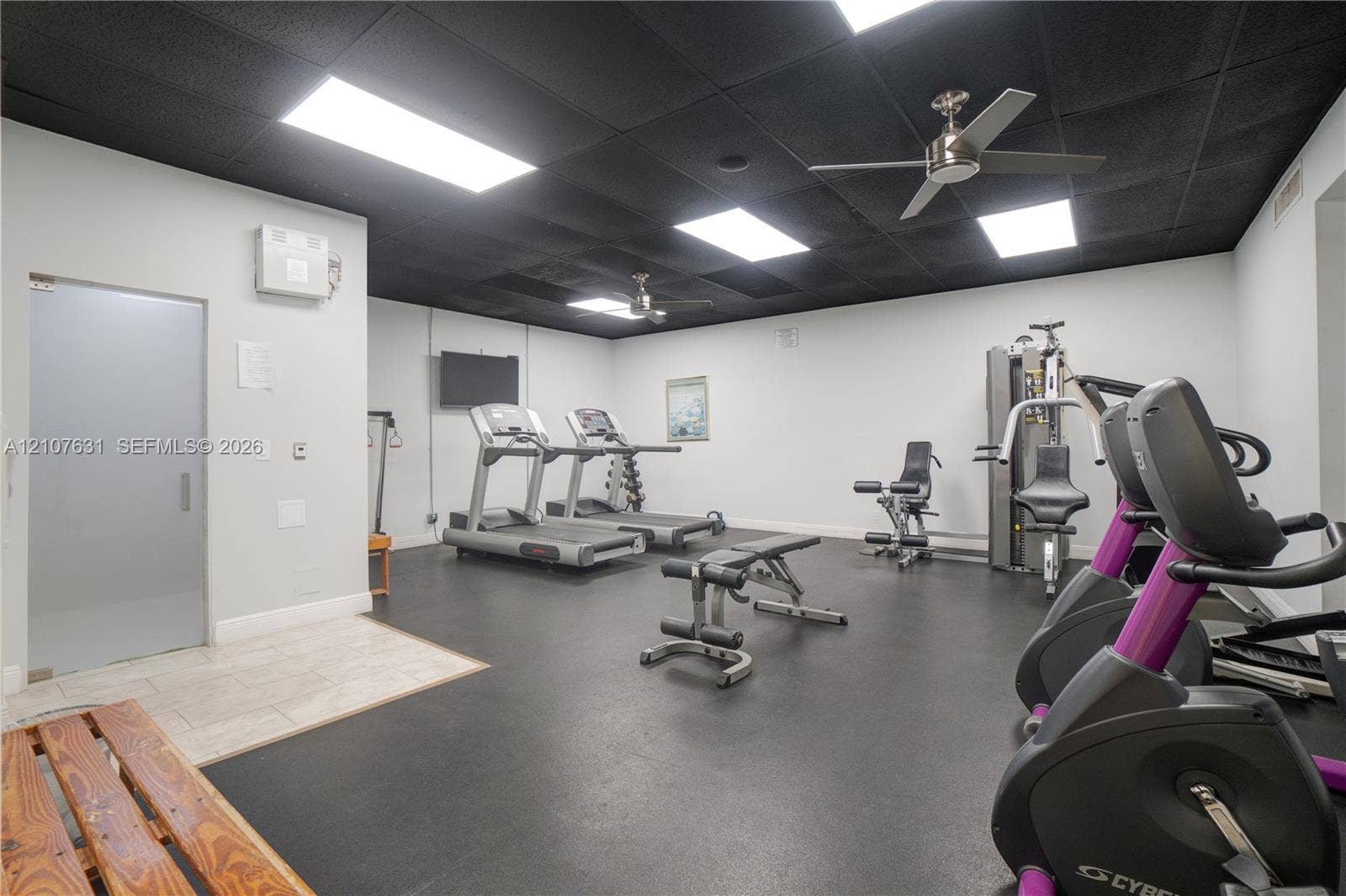 151 Berkley Road, #112, Hollywood, FL 33024 Fitness area featuring dark rubber flooring, black drop ceiling, recessed rectangular lighting, dual brushed-metal ceiling fans, and a glass-enclosed sauna room