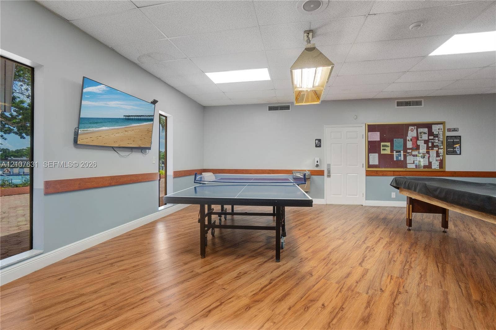 151 Berkley Road, #112, Hollywood, FL 33024 Recreation room featuring wood-finish flooring, a drop ceiling with recessed and pendant lighting, dual-tone walls with wood trim, and large windows