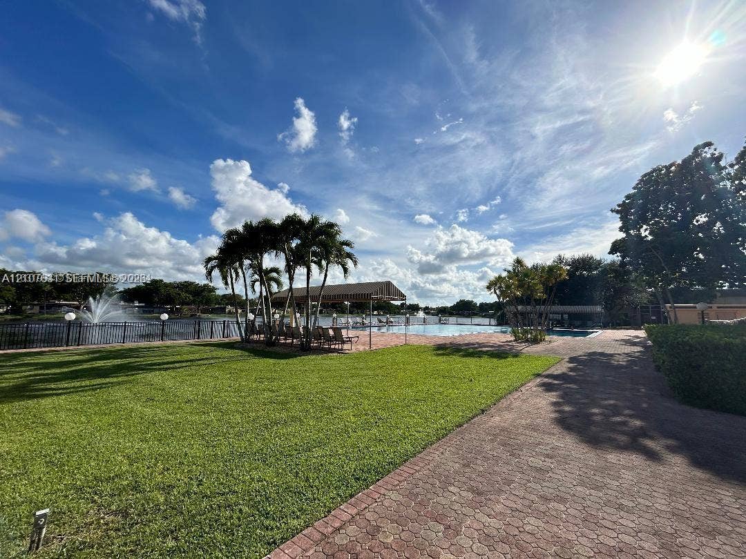 151 Berkley Road, #112, Hollywood, FL 33024 Waterfront outdoor space featuring a swimming pool, paved patio, expansive lawn, and mature palm trees