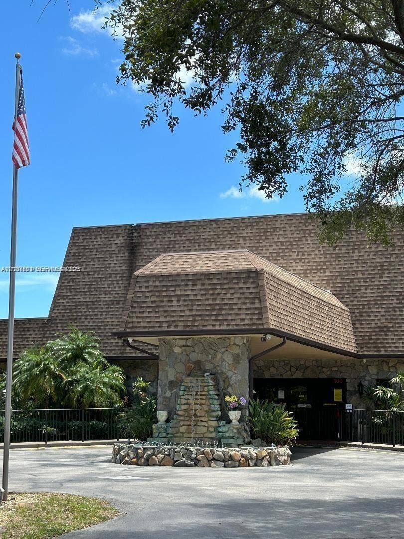 151 Berkley Road, #112, Hollywood, FL 33024 Exterior facade featuring a mansard roofline, decorative stone masonry, a built-in tiered stone fountain, and a paved circular driveway
