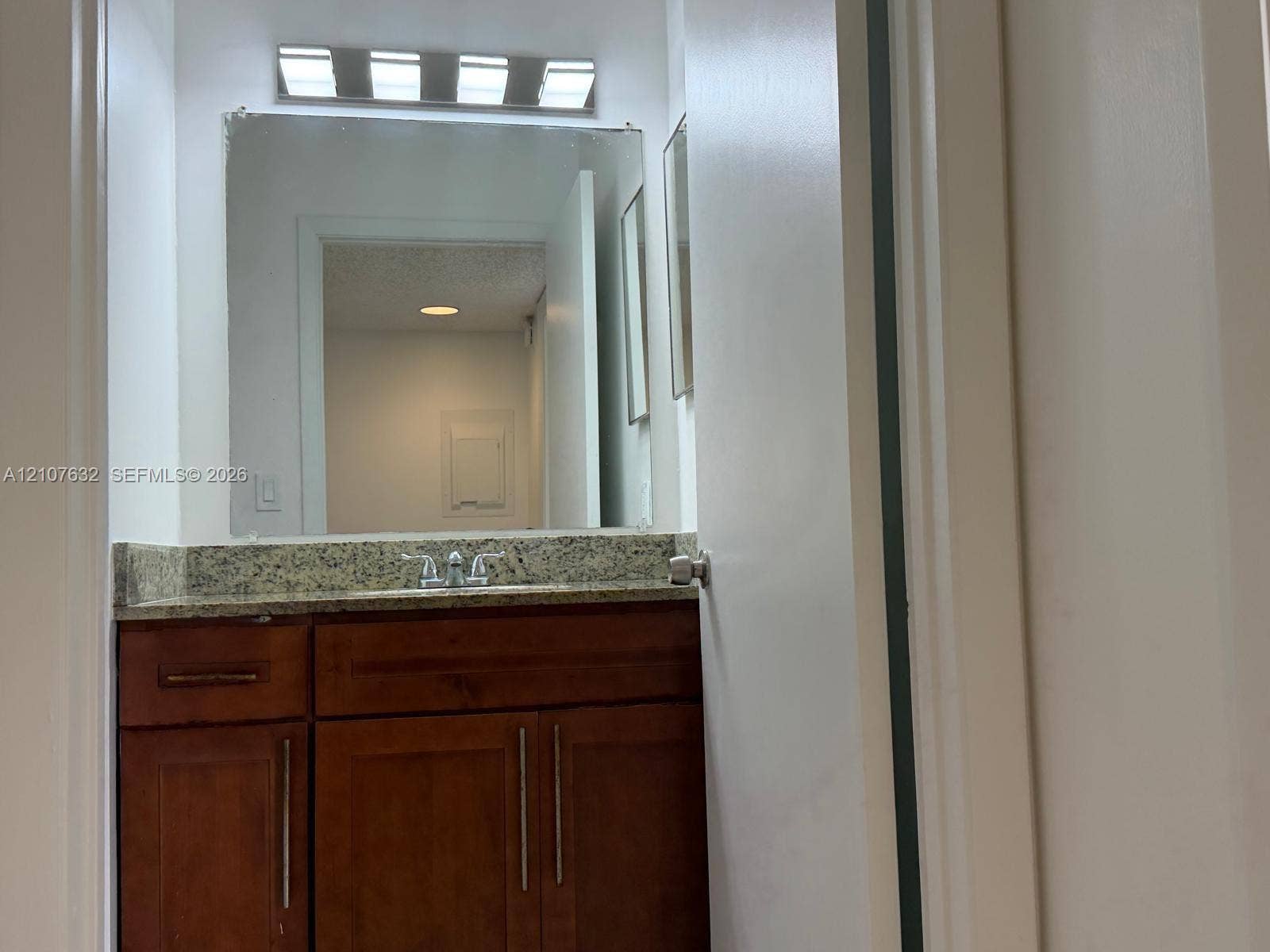 4501 W Mcnab Road, #13, Pompano Beach, Pompano Beach, FL 33069 Vanity featuring wood-finish cabinetry, stone countertop, integrated sink with dual-handle faucet, wall-mounted mirror, and four-bulb overhead lighting fixture